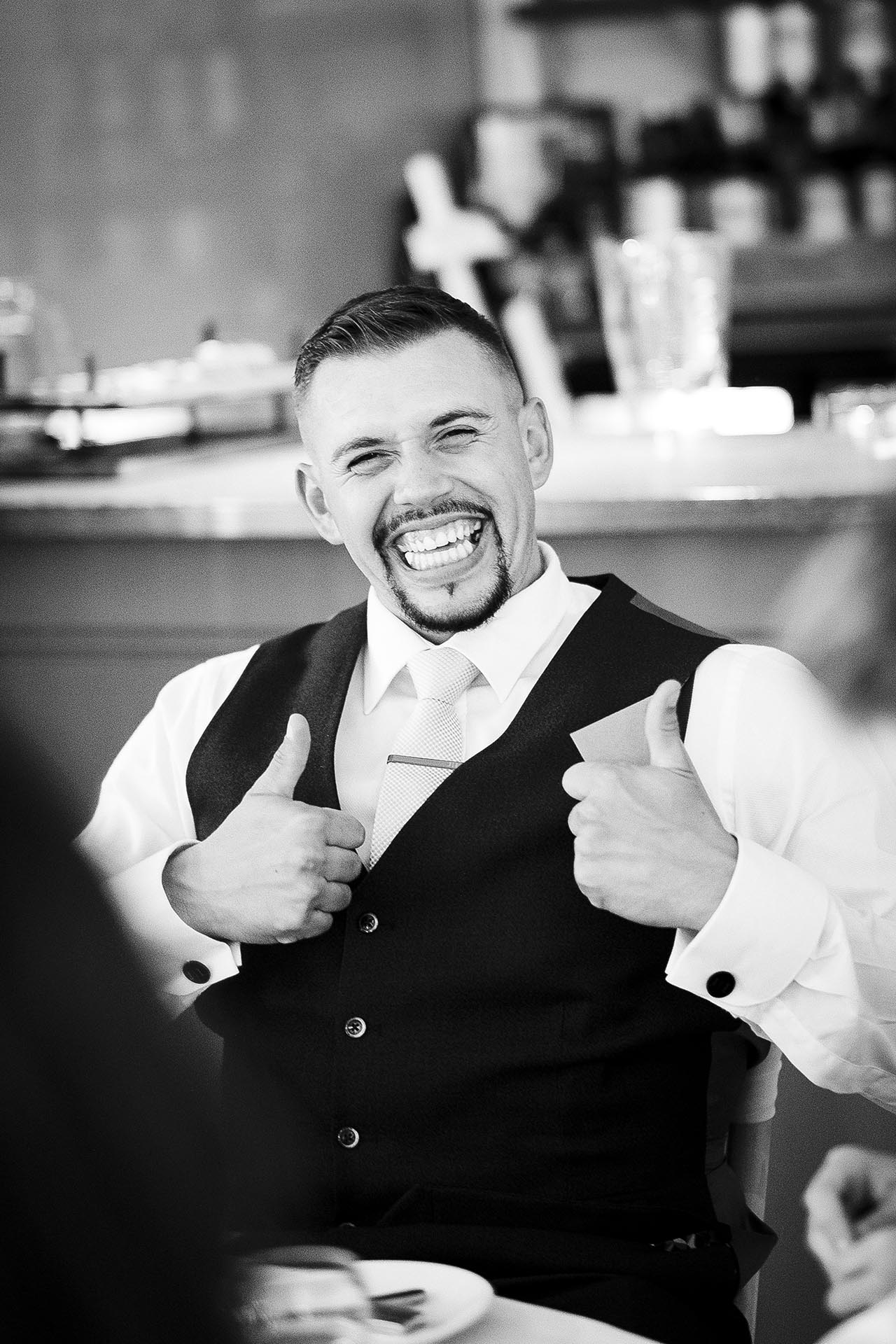 Black and white photograph of laughing guest with his thumbs up