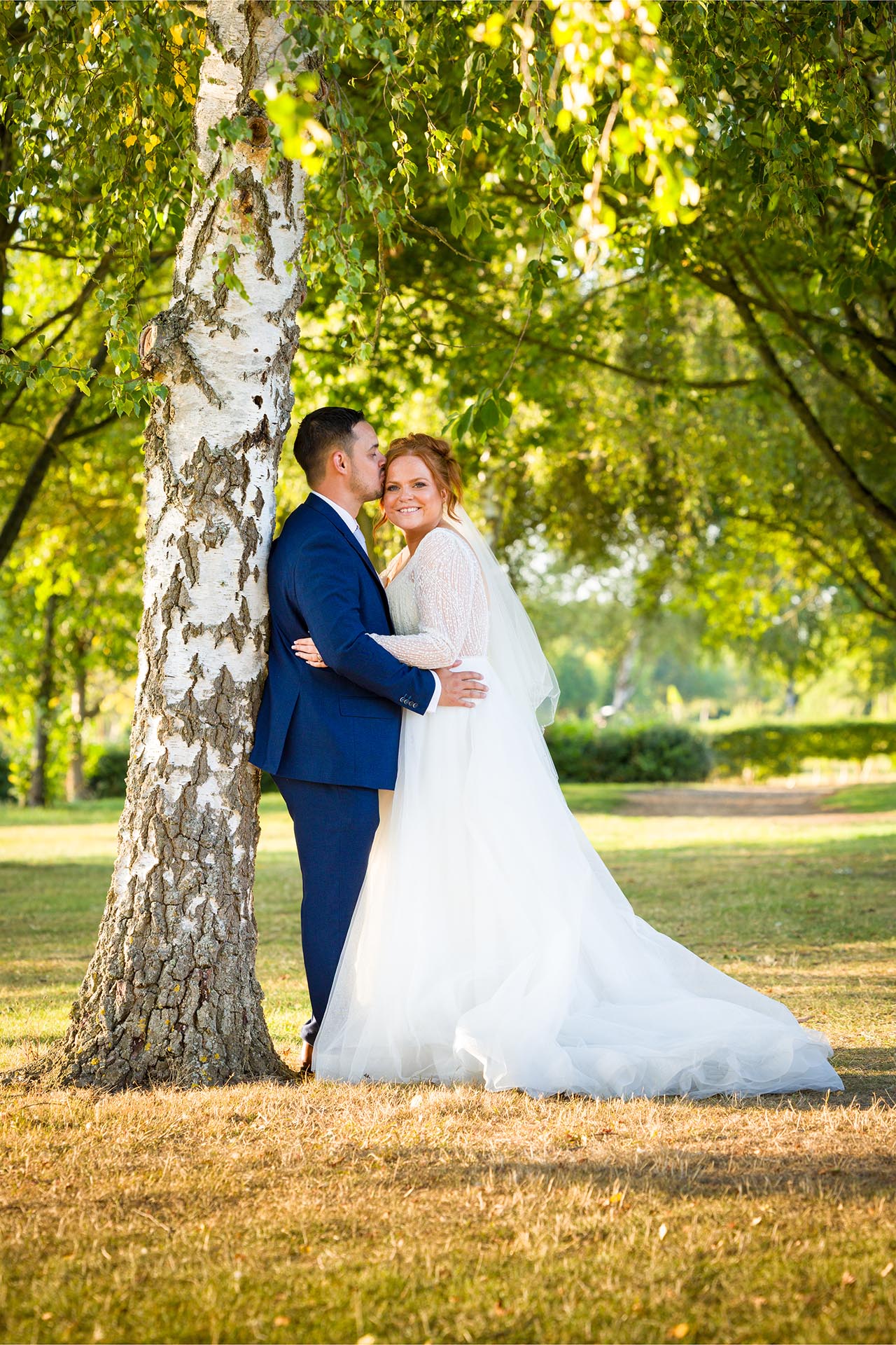 Groom leaning against a tree and kissing the bride in the late afternoon sun at Little Channels, Essex