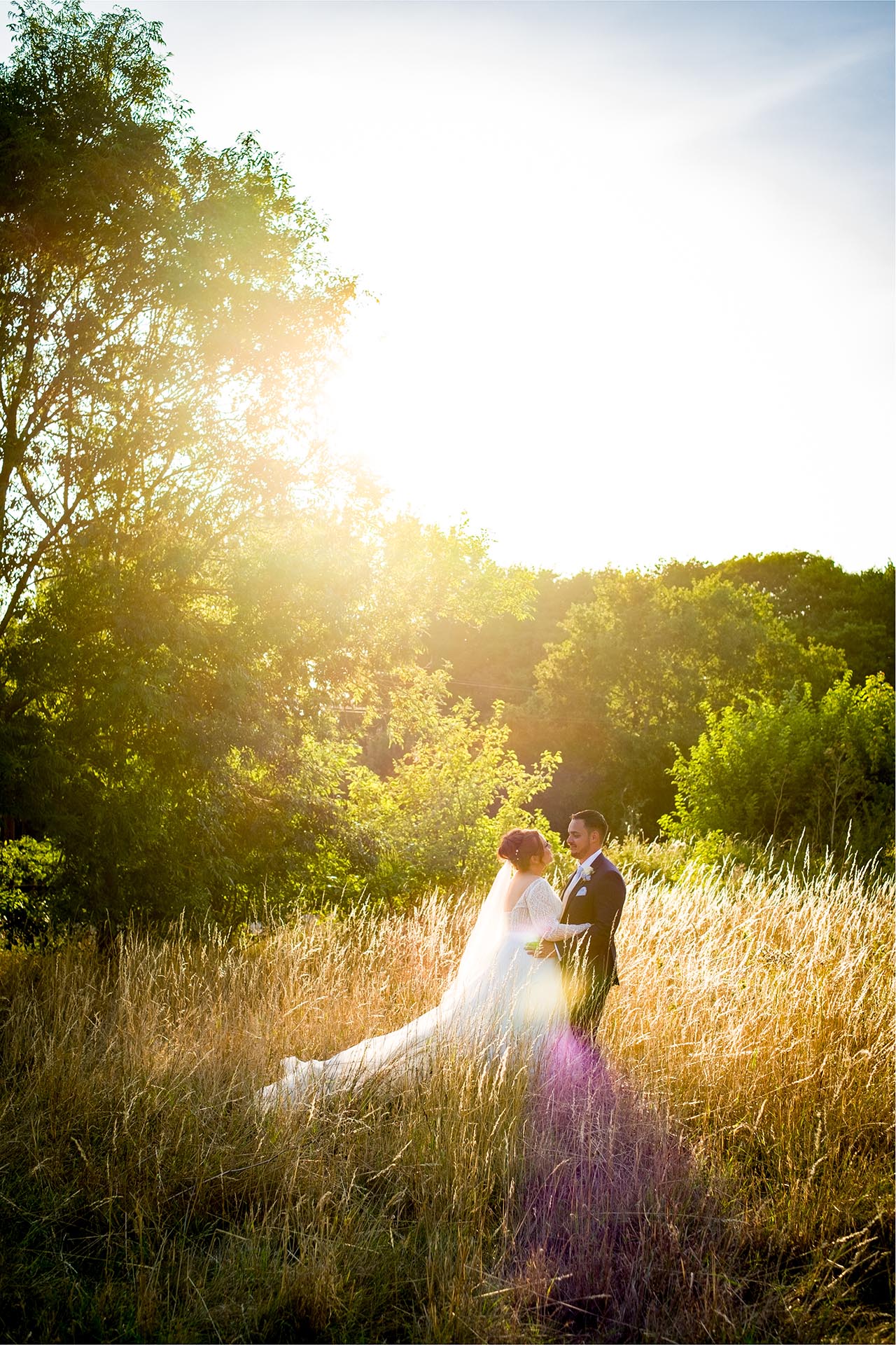 Bride and groom standing in long grass and looking at each other in the late afternoon sun at Little Channels, Essex