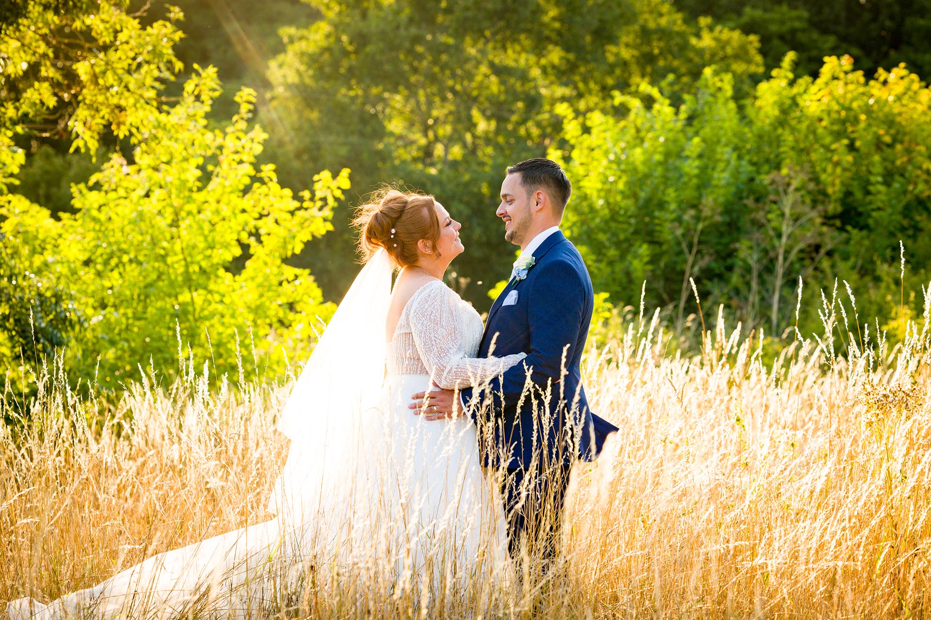 Bride and groom standing in long grass and looking at each other in the late afternoon sun at Little Channels, Essex