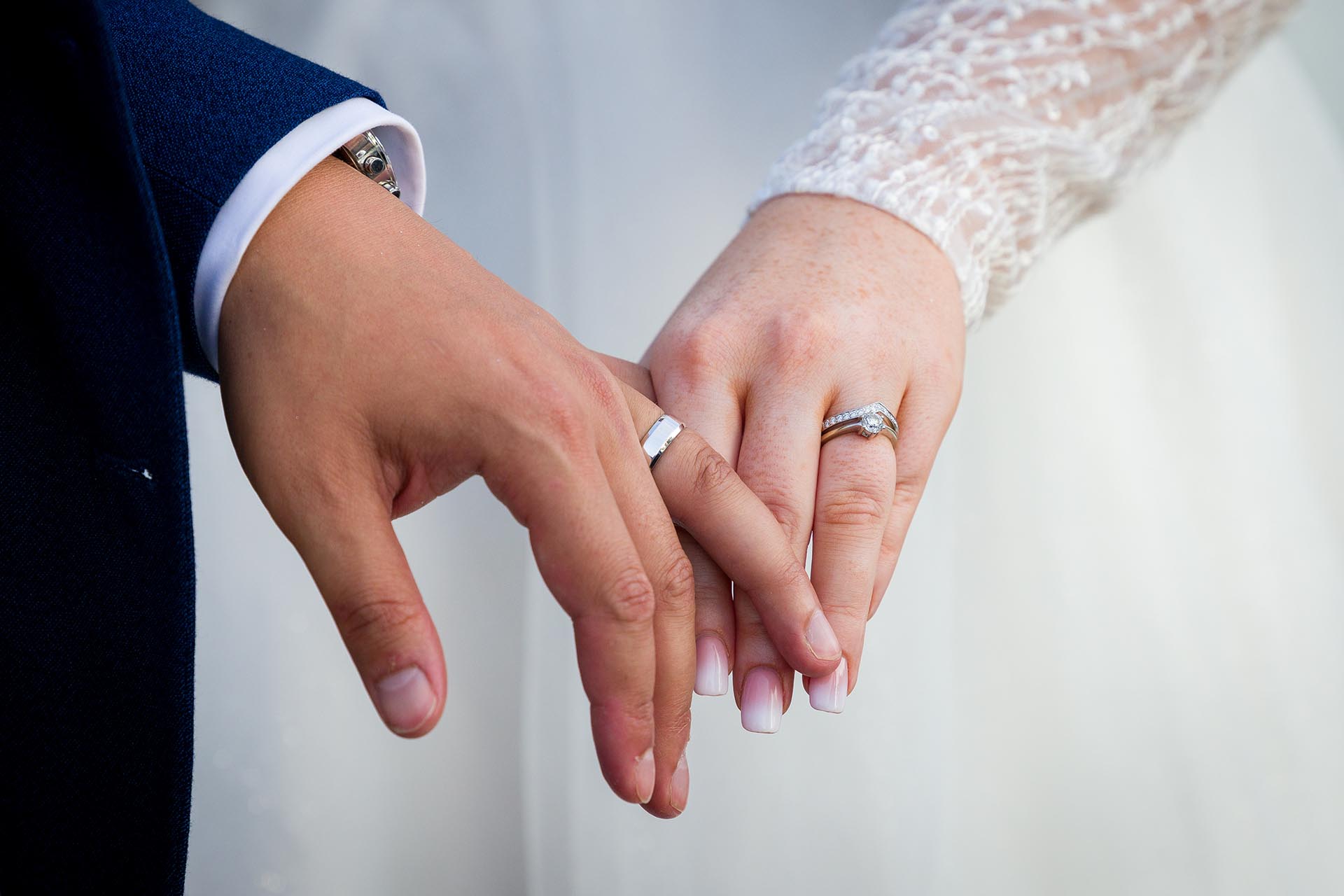 Close up photograph showing the wedding rings as the bride and groom hold hands