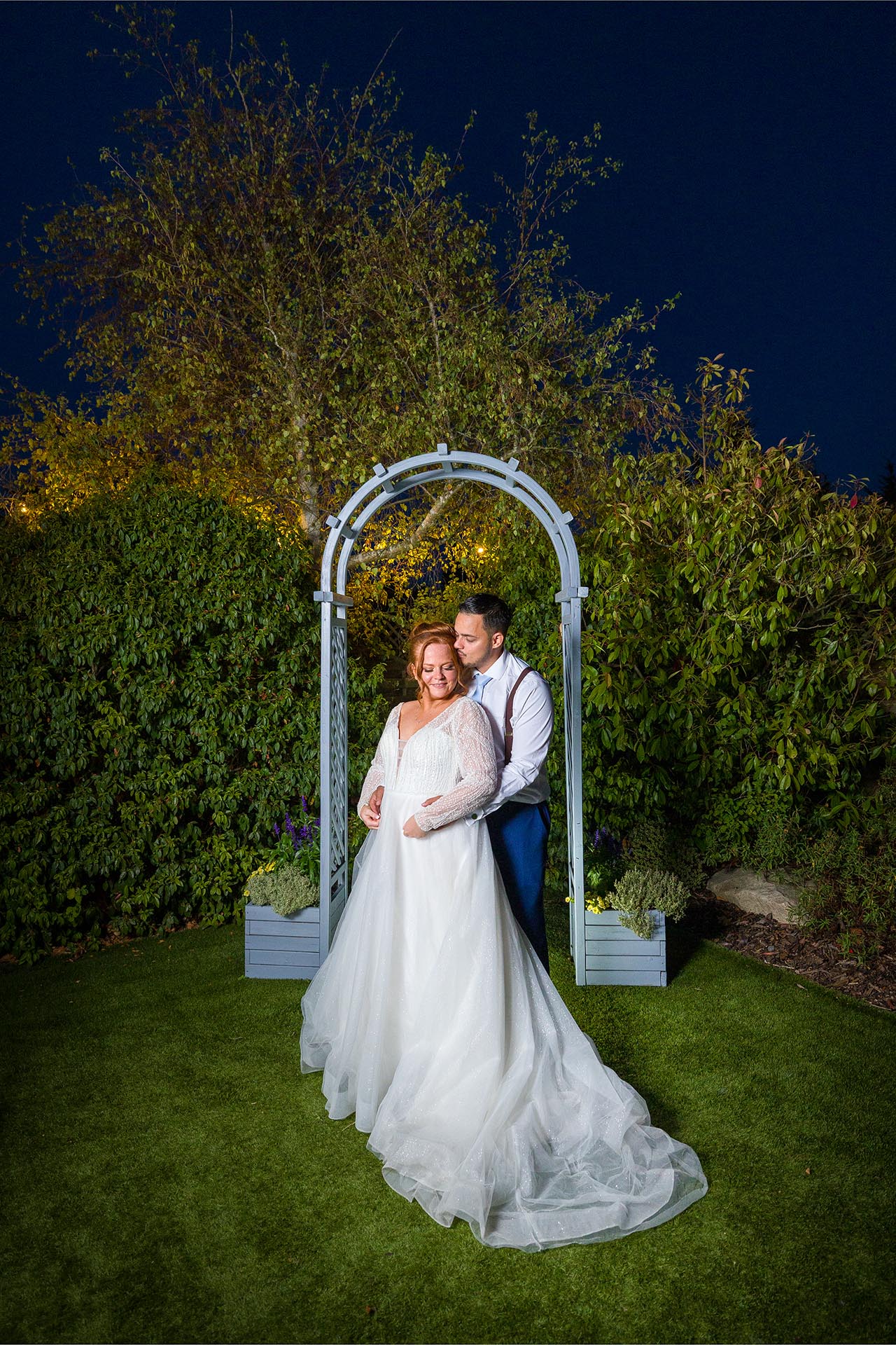 The bride and groom embraced at twilight under a garden arch at Little Channels, Essex